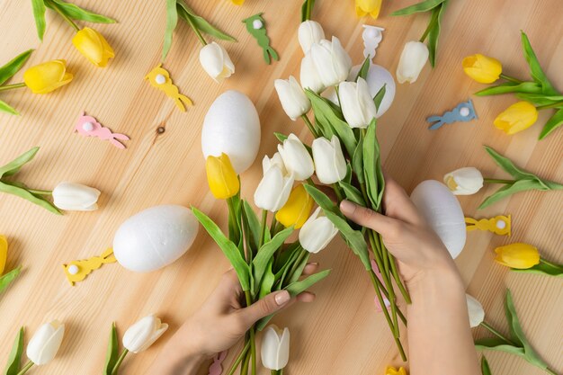 Mani femminili che tengono il mazzo di fiori freschi del tulipano bianco su fondo di legno, composizione piana laica con lo spazio della copia