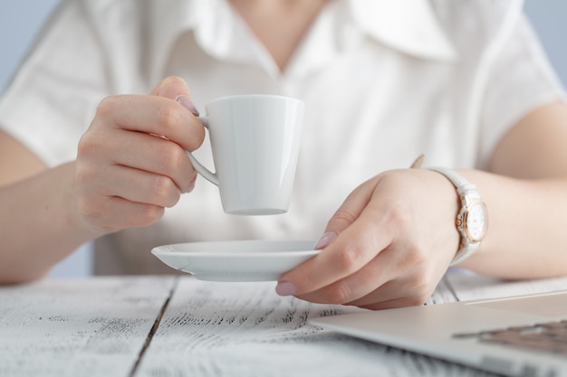 Mani femminili che tengono il primo piano della tazza di caffè. Computer portatile Gadget popolare, stile di vita moderno, vita aziendale, concetto di caffè del mattino