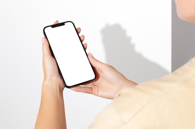 Mani femminili che tengono il telefono cellulare con schermo vuoto su sfondo bianco Mockup