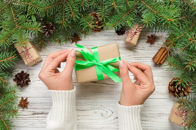 Mani femminili che tengono la scatola attuale fatta a mano in carta riciclata sul fondo della tavola in legno bianco. preparazione di Natale, sfondo confezione regalo