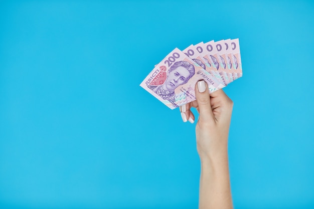Mani femminili che tengono le banconote ucraine sul blu