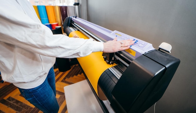 Mani femminili che tengono materiale stampabile giallo su plotter da stampa di grande formato Progettazione grafica e