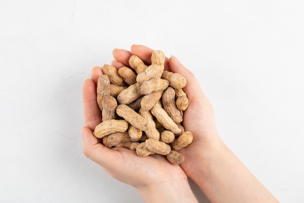 Mani femminili che tengono mazzo di arachidi organiche su superficie bianca.