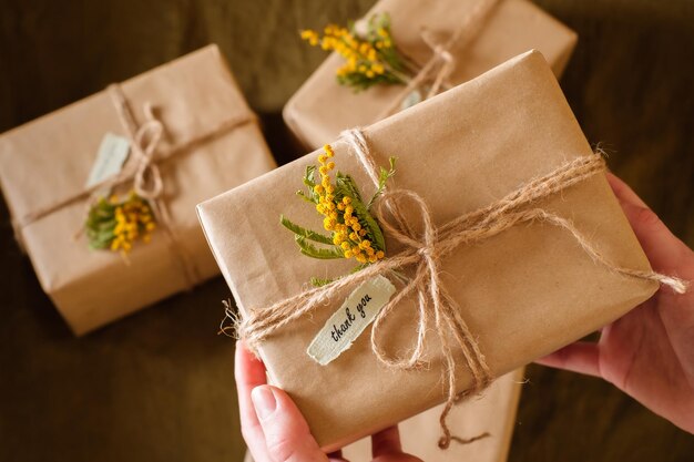 Mani femminili che tengono scatole regalo decorate con fiori gialli con parole di gratitudine