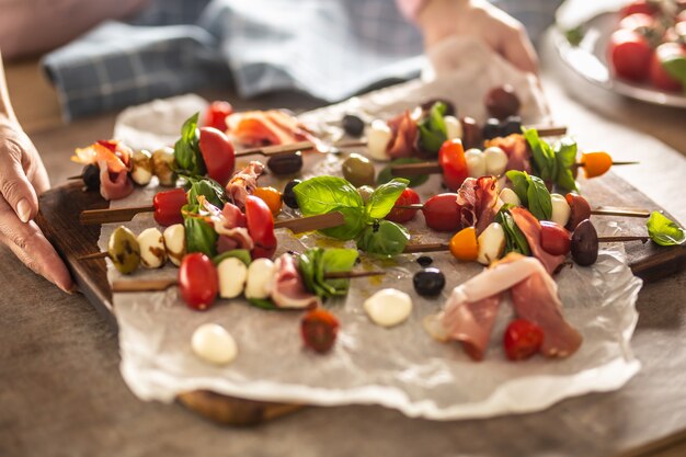 Mani femminili che tengono tavola con mini spiedini caprese antipasto italiano o mediterraneo