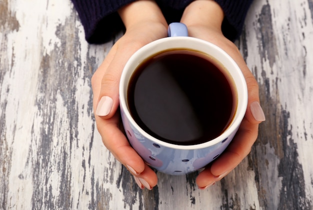 Mani femminili che tengono tazza di caffè su fondo di legno