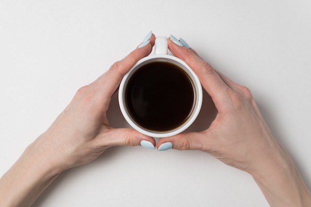 Mani femminili che tengono tazza di caffè su superficie bianca. Tazza di tè in mani femminili.