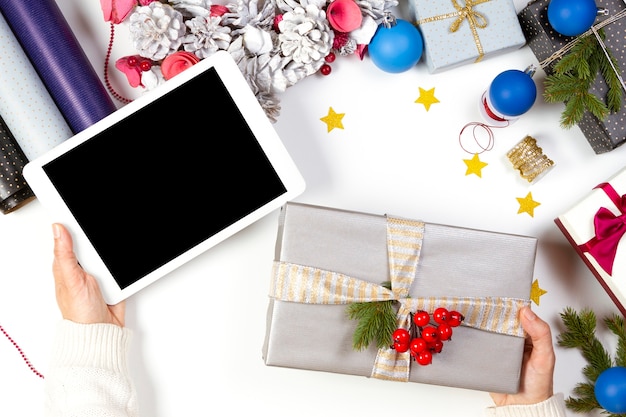 Mani femminili che tengono un computer tablet e un regalo di Natale presente su sfondo bianco