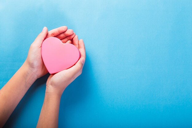 Mani femminili che tengono un cuore rosa su sfondo azzurro.