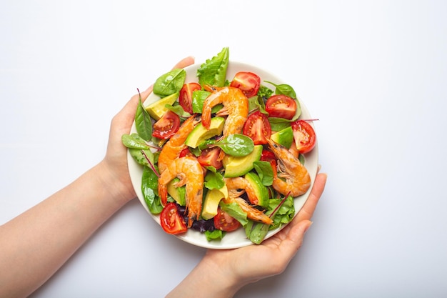 Mani femminili che tengono un'insalata sana con gamberetti alla griglia