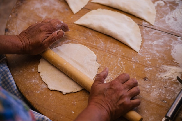 Mani femminili che tengono un mattarello nel processo di cottura di kutaba o chebureks carne macinata e cipolle in pastaCottage e cipolla nell'impasto Cucina greca caucasica tartara azerbaigiana