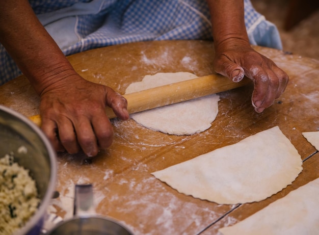 Mani femminili che tengono un mattarello nel processo di cottura di kutaba o chebureks carne macinata e cipolle in pastaCottage e cipolla nell'impasto Cucina greca caucasica tartara azerbaigiana