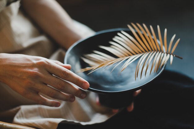 Mani femminili che tengono un piatto ceramico nero decorato con il primo piano della foglia di felce