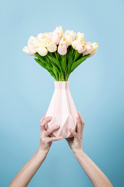 Mani femminili che tengono un vaso con un mazzo di tulipani su sfondo blu