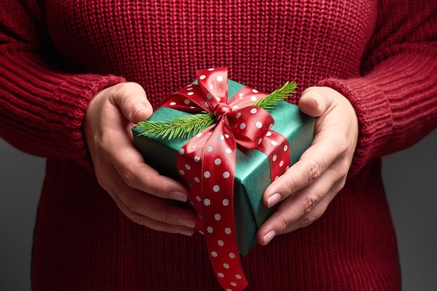 Mani femminili che tengono una scatola regalo di natale decorata con fiocco rosso