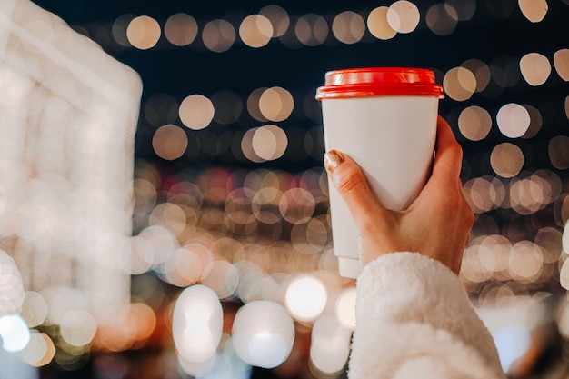 Mani femminili che tengono una tazza di caffè caldo Luci di ghirlanda di Bokeh Dettagli magici delle vacanze di Natale