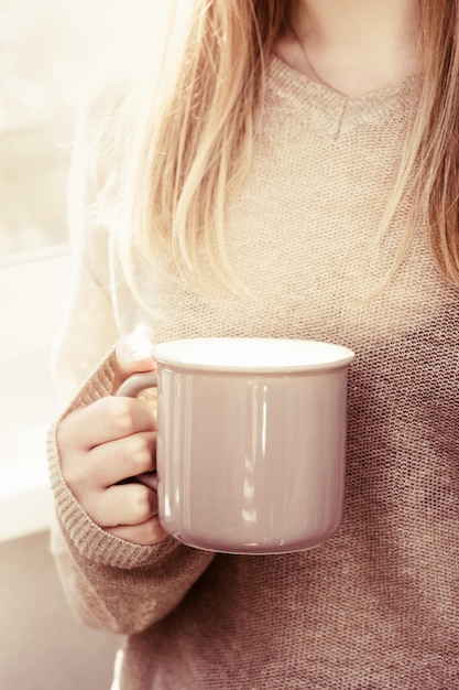 Mani femminili che tengono una tazza di caffè o tè calda alla luce del sole del mattino Bevande mormoranti e buon umore