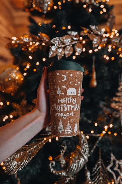 Mani femminili che tengono una tazza di caffè o tè con un design accogliente di Natale Decorazioni per le vacanze invernali