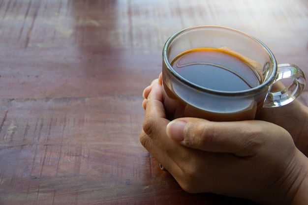 Mani femminili che tengono una tazza di caffè sopra il tavolo in legno