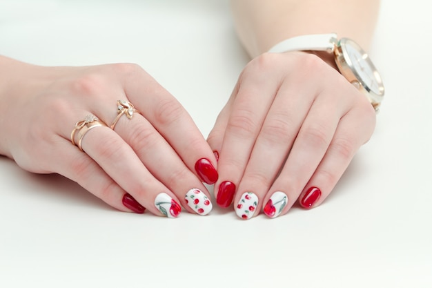 Mani femminili con manicure, smalto rosso, disegno con ciliegie. Orologio da polso. Sfondo bianco.