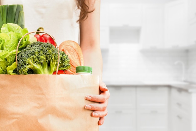 Mani femminili con sacchetto di carta di generi alimentari sullo sfondo della cucina