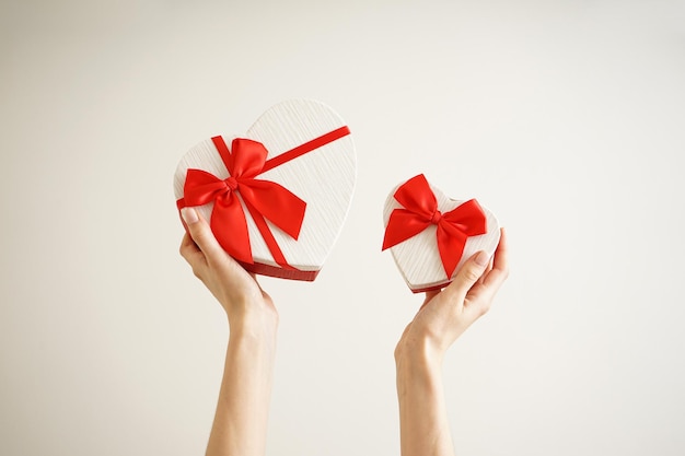 Mani femminili con scatole regalo per San Valentino su uno sfondo colorato.
