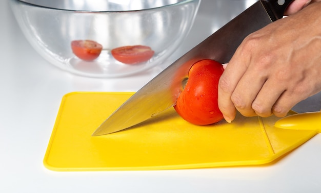 Mani femminili con un coltello tagliano un pomodoro su un tagliere giallo