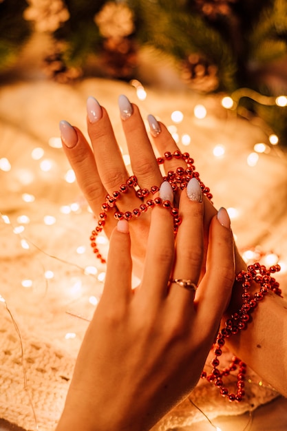 Mani femminili con una ghirlanda natalizia di perline rosse su uno sfondo di rami di pino