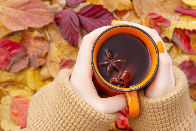 Mani femminili con una tazza di caffè arancione su sfondo foglie autunnali