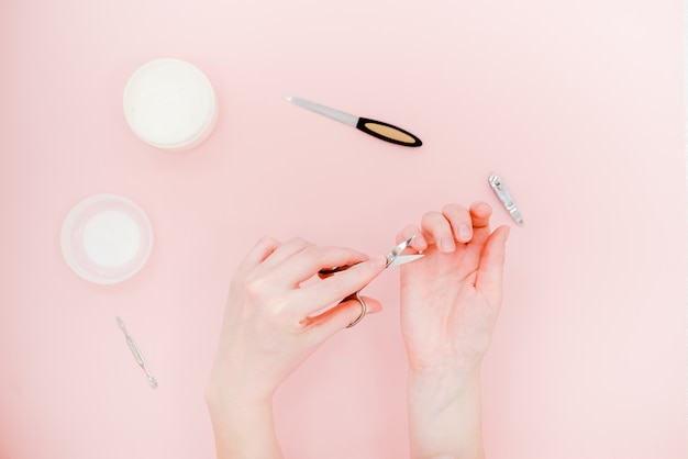 Mani femminili con vaso bianco crema e kit manicure, forbici, lucidante.