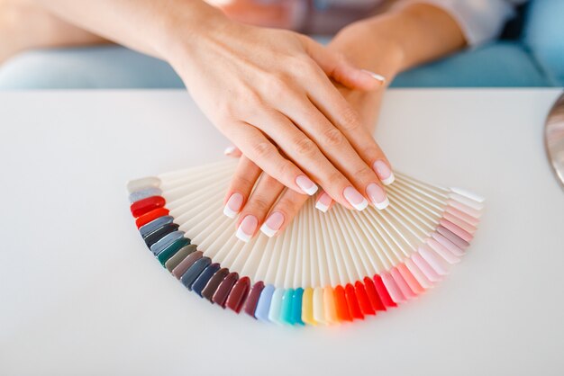 Mani femminili del cliente e tavolozza di smalto colorato per unghie nel salone di bellezza.