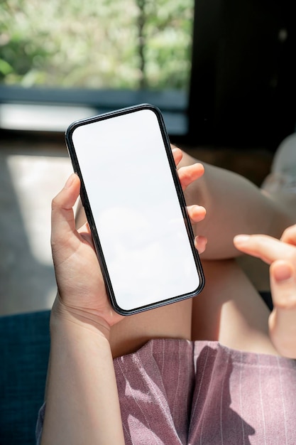 Mani femminili del primo piano che utilizzano smartphone a casa. Telefono cellulare a schermo vuoto per il montaggio del display grafico.