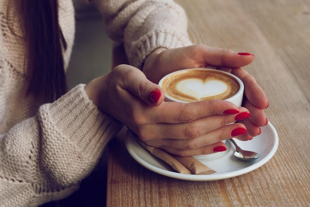 Mani femminili del primo piano con la tazza rossa della tenuta del manicure dello smalto del gel con caffè