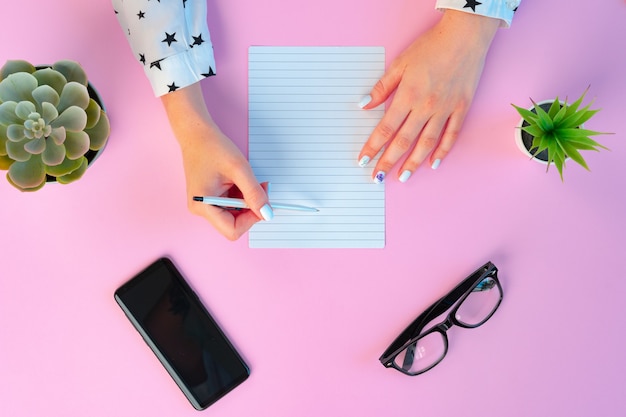 Mani femminili e blocco note aperto sulla vista superiore rosa