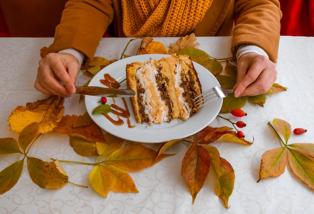 Mani femminili e piastra con torta sul tavolo con foglie di autunno