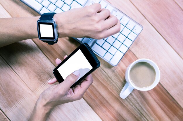 Mani femminili facendo uso dello smartphone e dell&#39;orologio astuto con caffè e tastiera sul tavolo