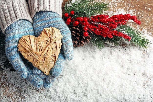 Mani femminili in guanti blu con cuore decorativo su sfondo di neve