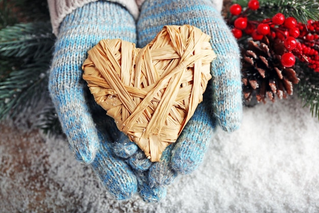 Mani femminili in guanti blu con cuore decorativo su sfondo di neve