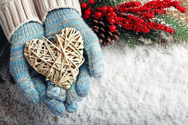 Mani femminili in guanti blu con cuore decorativo su sfondo di neve