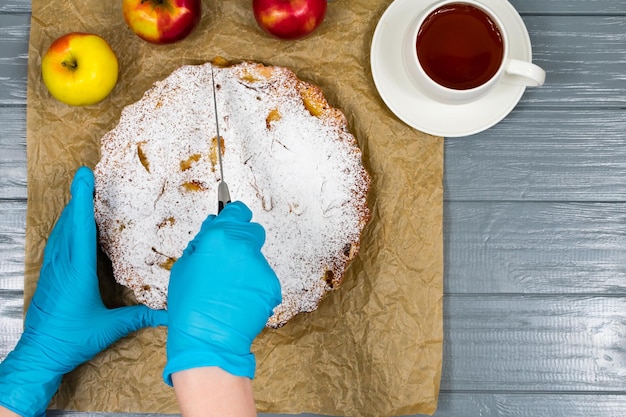 Mani femminili in guanti blu tagliano a pezzi una torta di mele