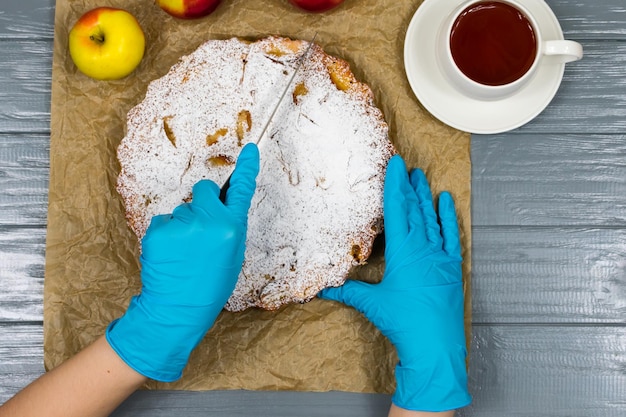 Mani femminili in guanti blu tagliano a pezzi una torta di mele