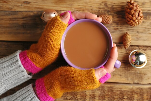 Mani femminili in guanti che tengono tazza di caffè su fondo di legno