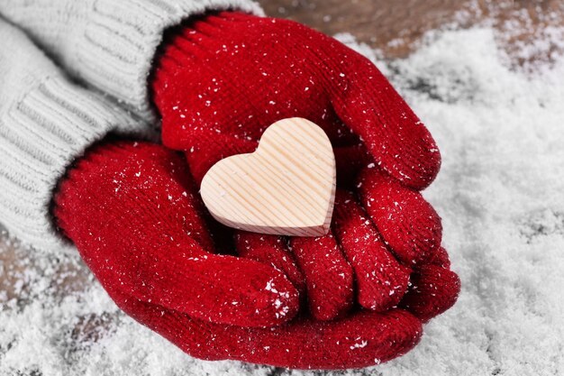 Mani femminili in guanti con cuore decorativo su sfondo di neve