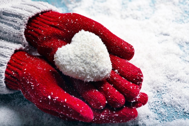 Mani femminili in guanti con cuore decorativo su sfondo di neve