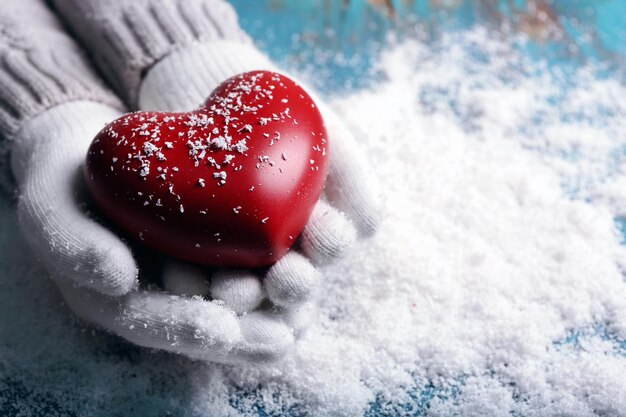 Mani femminili in guanti con cuore decorativo su sfondo di neve