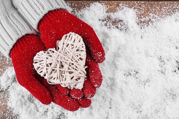 Mani femminili in guanti con cuore decorativo su sfondo di neve