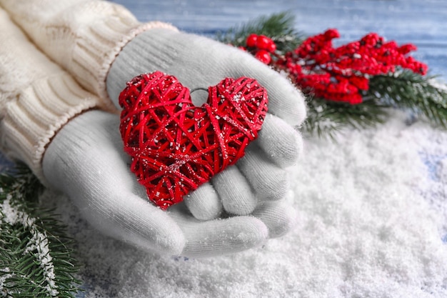 Mani femminili in guanti con cuore decorativo su sfondo di neve