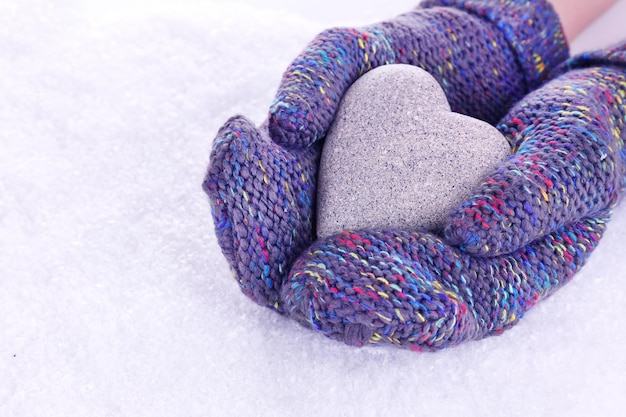 Mani femminili in guanti con cuore su sfondo di neve