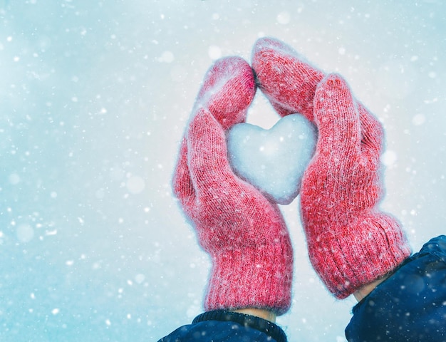 mani femminili in guanti lavorati a maglia con cuore di neve nella giornata invernale. Concetto di amore.