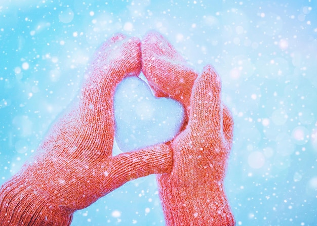Mani femminili in guanti lavorati a maglia con cuore di neve nella giornata invernale. concetto.